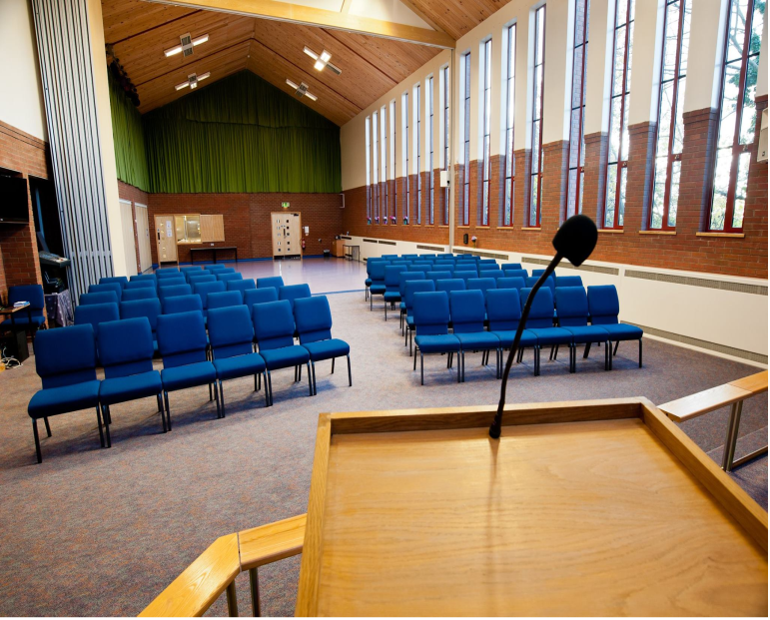 interior of St Peter's church Glascote Heath - a view from a plain wooden pulpit of the modern building with many tall clear windows, room partition, high wooden ceiling and blue chairs