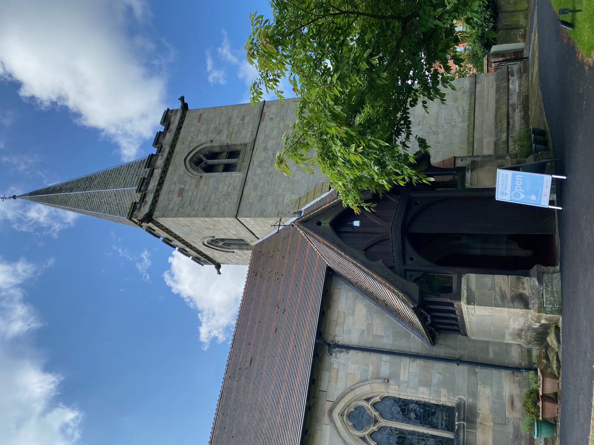 The outside of St Michael's church, Rocester, with the spire and a Places of Welcome sign at the entrance