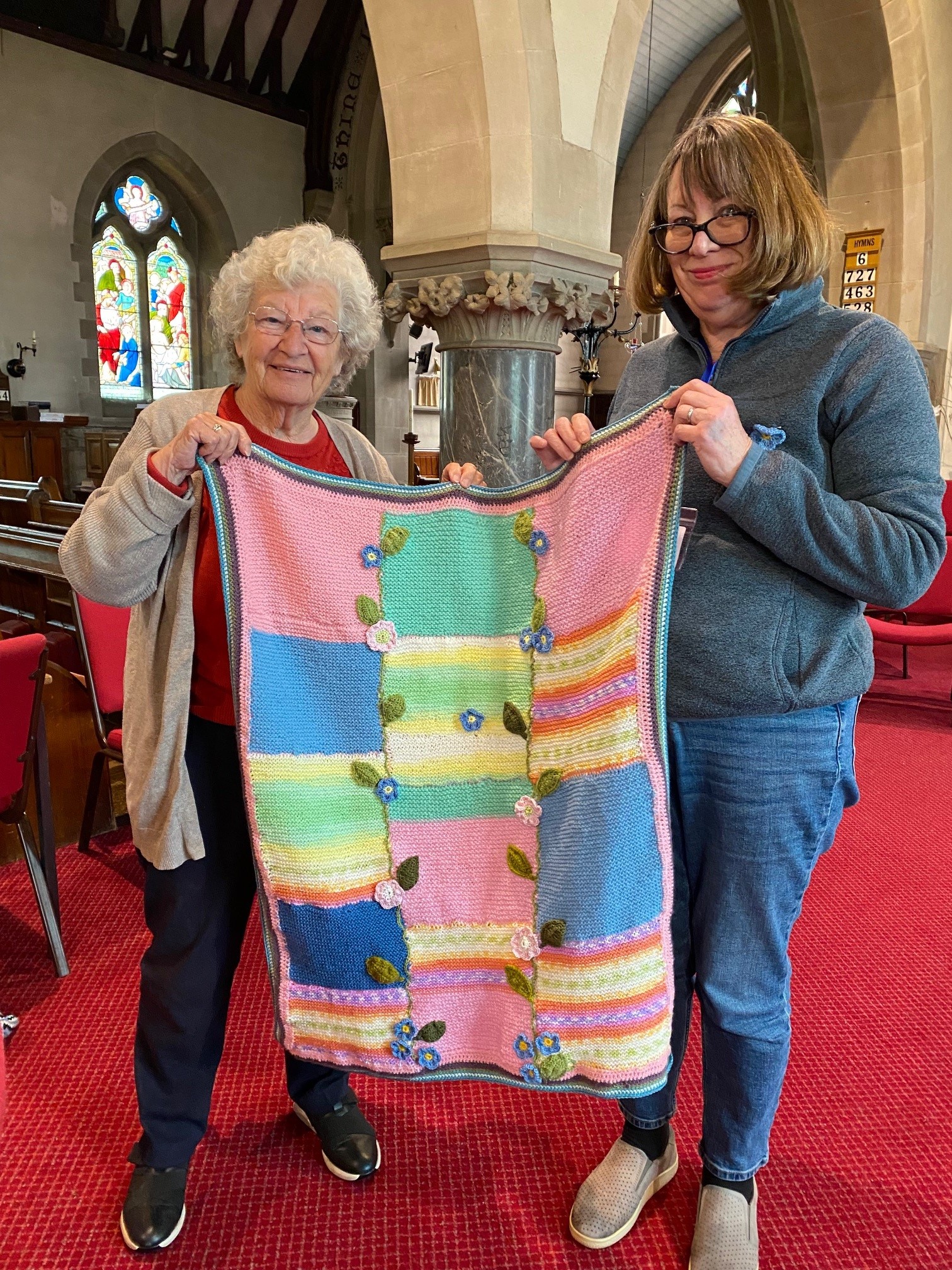 Two ladies holding up the knitted blanket