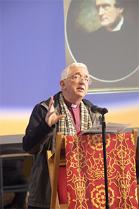 Bishop Michael speaking at the 2024 Selwyn Lecture with a picture of Bishop Selwyn behind him
