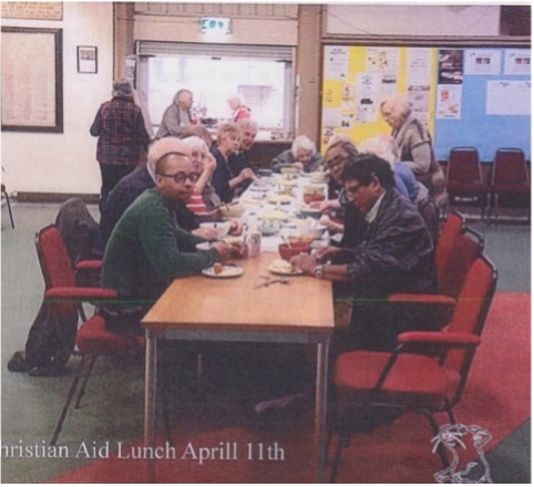 A group sitting along a table in the church hall sharing lunch
