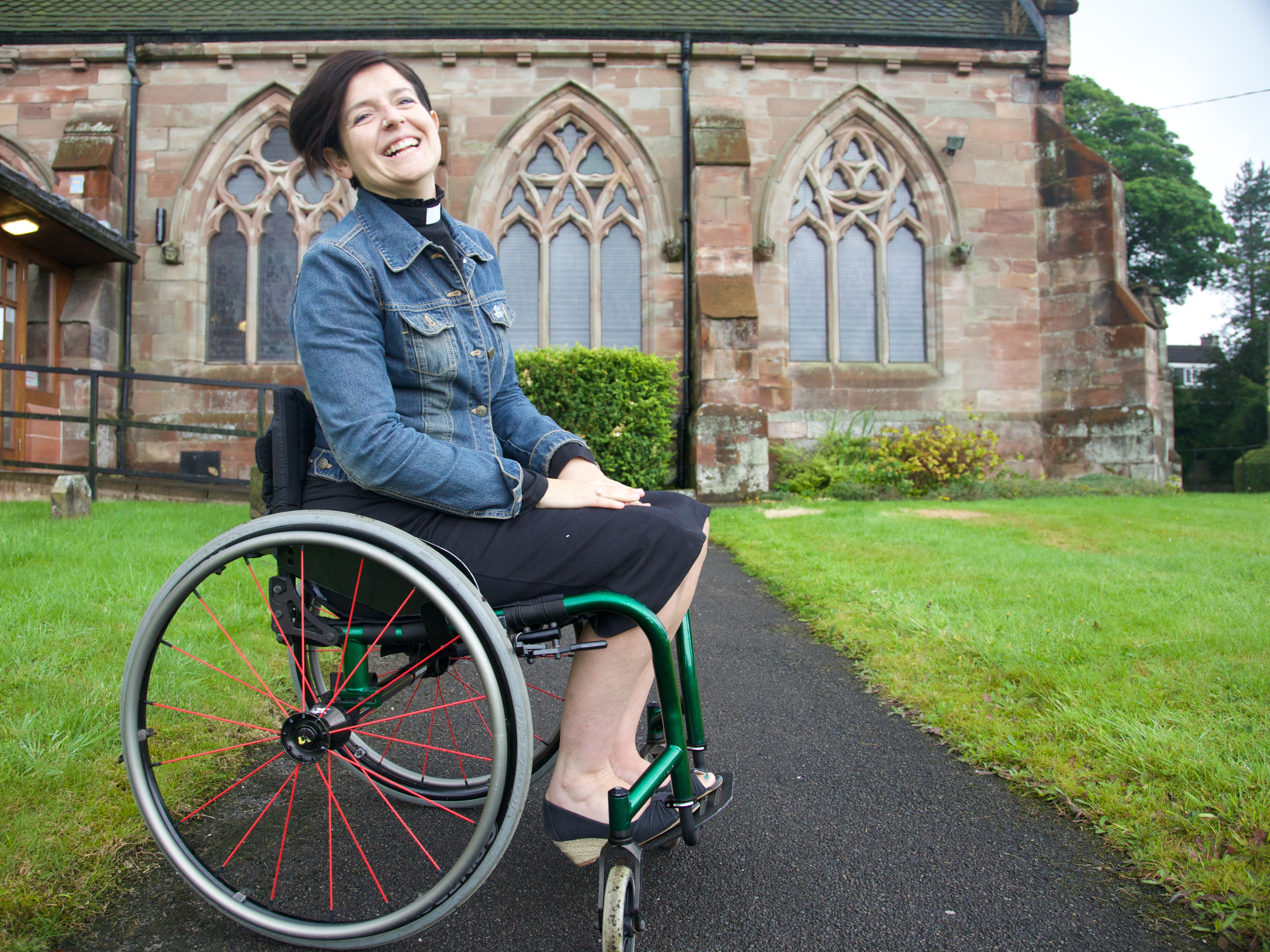 Revd Zoe Hemmings, laughing, sat in her wheelchair outside a church